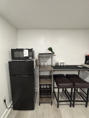 A compact kitchen with a refrigerator, microwave, and a small dining area with a bench. - Renovated Private Studio in Greer – Parking, Near Airport & BMW, Prime Location. (Greer)