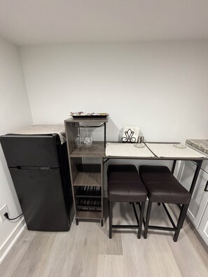 Eine kompakte Küche mit einem schwarzen Kühlschrank, einem kleinen Esstisch mit zwei Bänken und einem Regal mit Weingläsern.