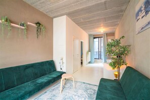 A living room with a green sofa, a small stool, and a plant on a shelf. - Antwerp Central One Bedroom Apartment (Antwerp)