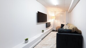 A modern living room with a flat-screen TV, a sofa, a floor lamp, and a small plant. - Bayview Aparthotel by Guestz (Morecambe)