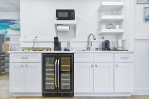Une cuisine moderne avec des meubles blancs, un four à micro-ondes encastré, un réfrigérateur et une machine à café.