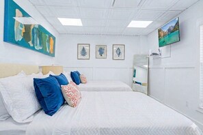 Une chambre d’hôtel avec deux lits, une grande peinture abstraite, des œuvres d’art représentant des feuilles encadrées, une télévision et un miroir.