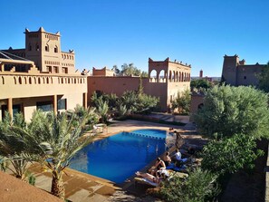 Zona de piscina con palmeras, cielo azul despejado y arquitectura tradicional.