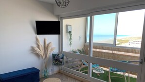 A room with a large window, a blue sofa, a small round table, and a chair with a tropical print cushion. - The horizon - Ocean view with magnificent sunset (Saint-Hilaire-de-Riez)