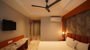 A hotel room with a bed, a bench, a ceiling fan, an air conditioning unit, and a television on the wall. - Bidesh Ghar Hotel (Puri)