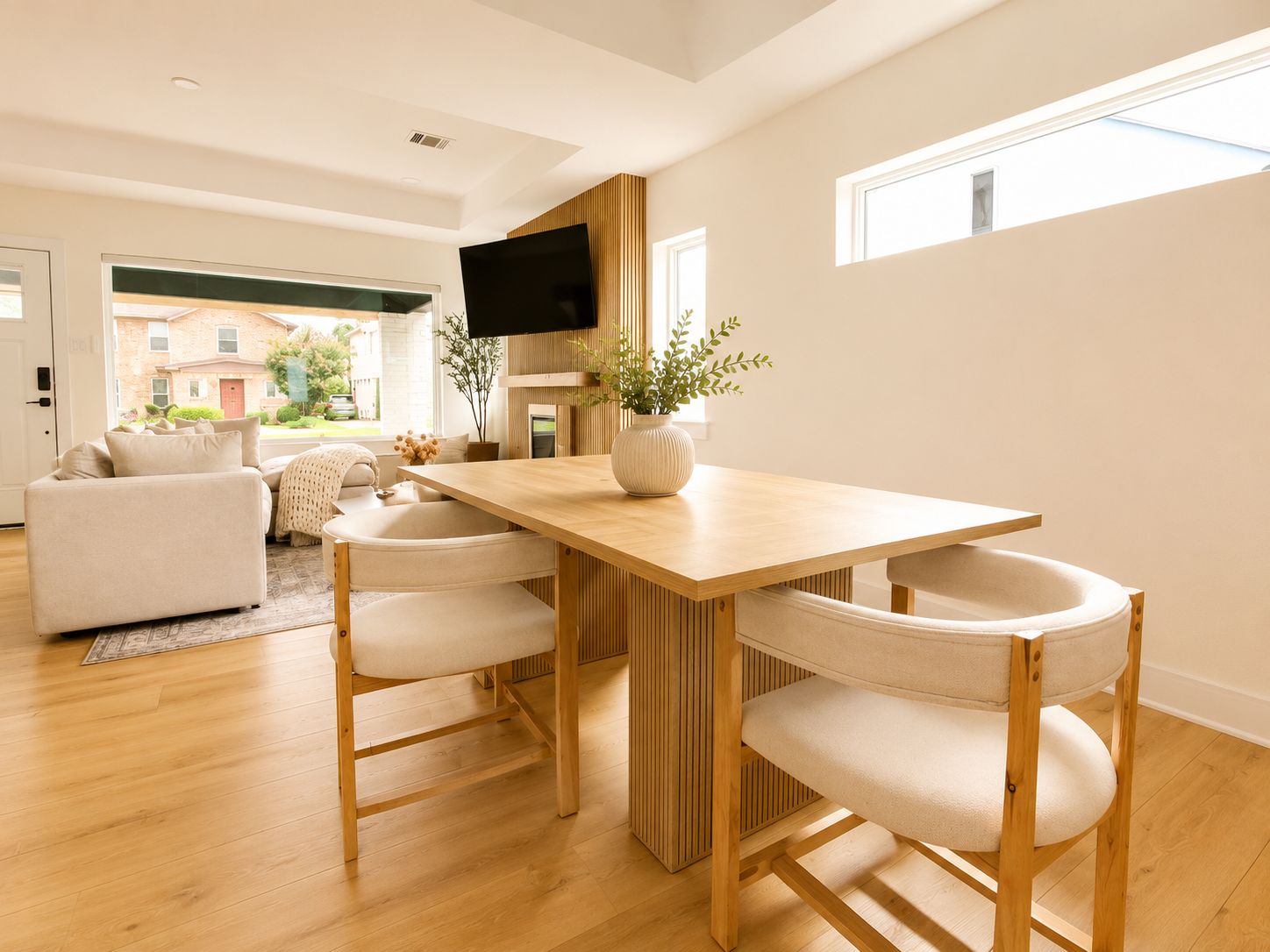 A modern living room with a wooden dining table, two chairs, a sofa, and a TV.