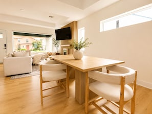 A modern living room with a wooden dining table, two chairs, a sofa, and a TV. - Muse Atelier | Houston (Houston)