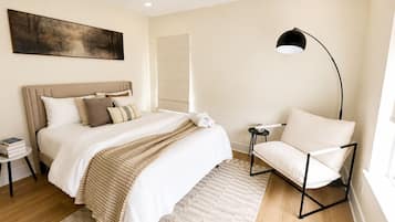 A bedroom with a bed, bedside tables, a chair, a floor lamp, and a painting on the wall.