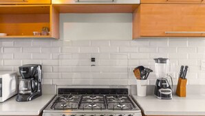 A kitchen with a gas stove, a coffee maker, a blender, and wooden cabinets. - Nice City View Apartment in Escalon! (San Salvador)