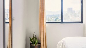 A bedroom with a bed, a window with curtains, a potted plant, and a mirror. - Nice City View Apartment in Escalon! (San Salvador)