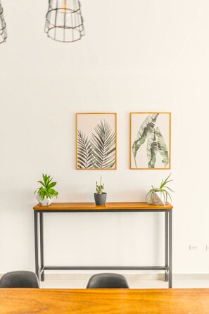 A minimalist room with a wooden console table, two framed leaf artworks, and three potted plants.