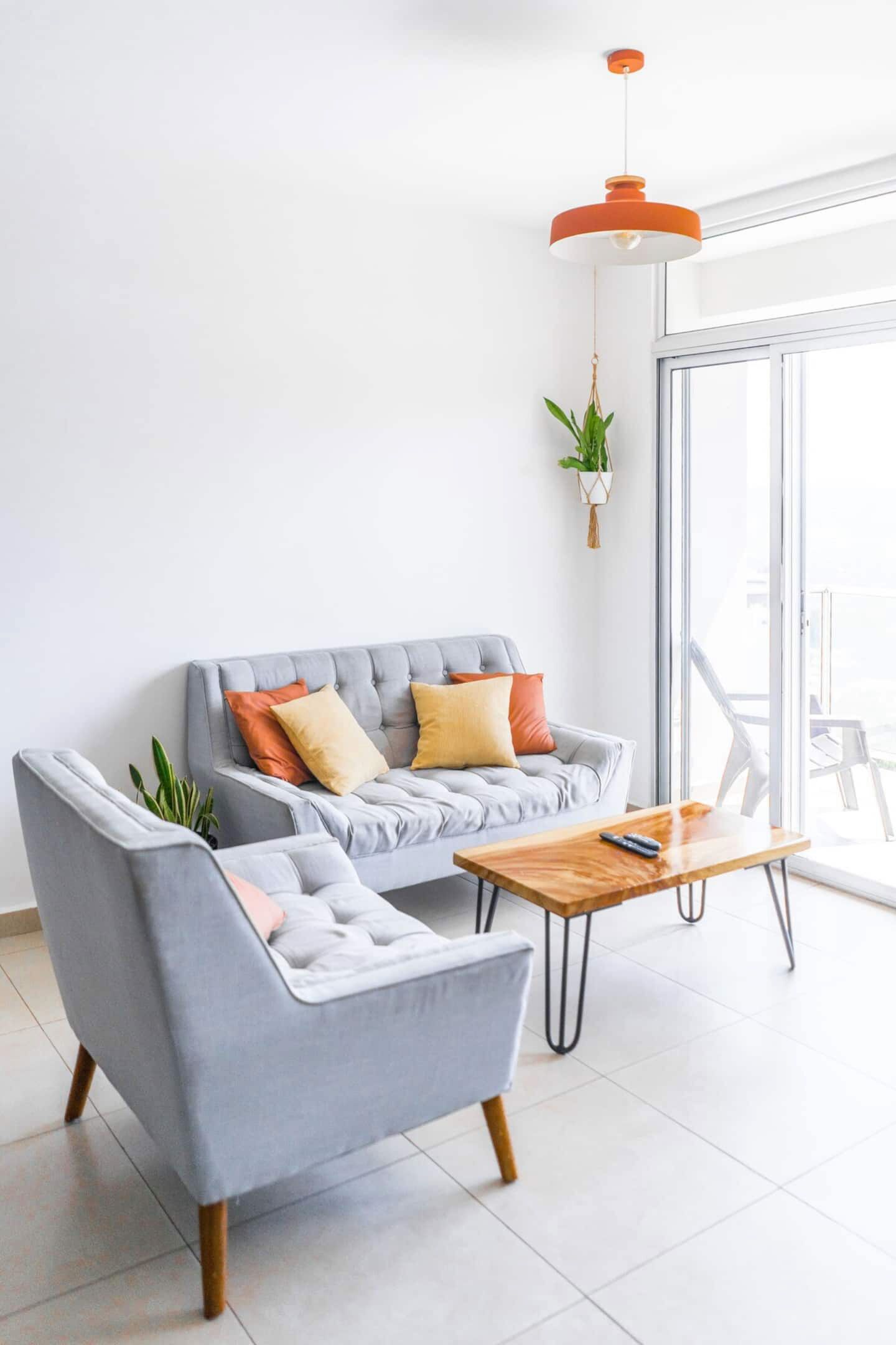 Una sala de estar moderna con un sofá gris, una mesa de centro de madera y una lámpara colgante naranja.
