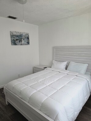 Une chambre à coucher comprenant un lit, une table de chevet, une œuvre d’art accrochée au mur et un luminaire fixé au plafond.