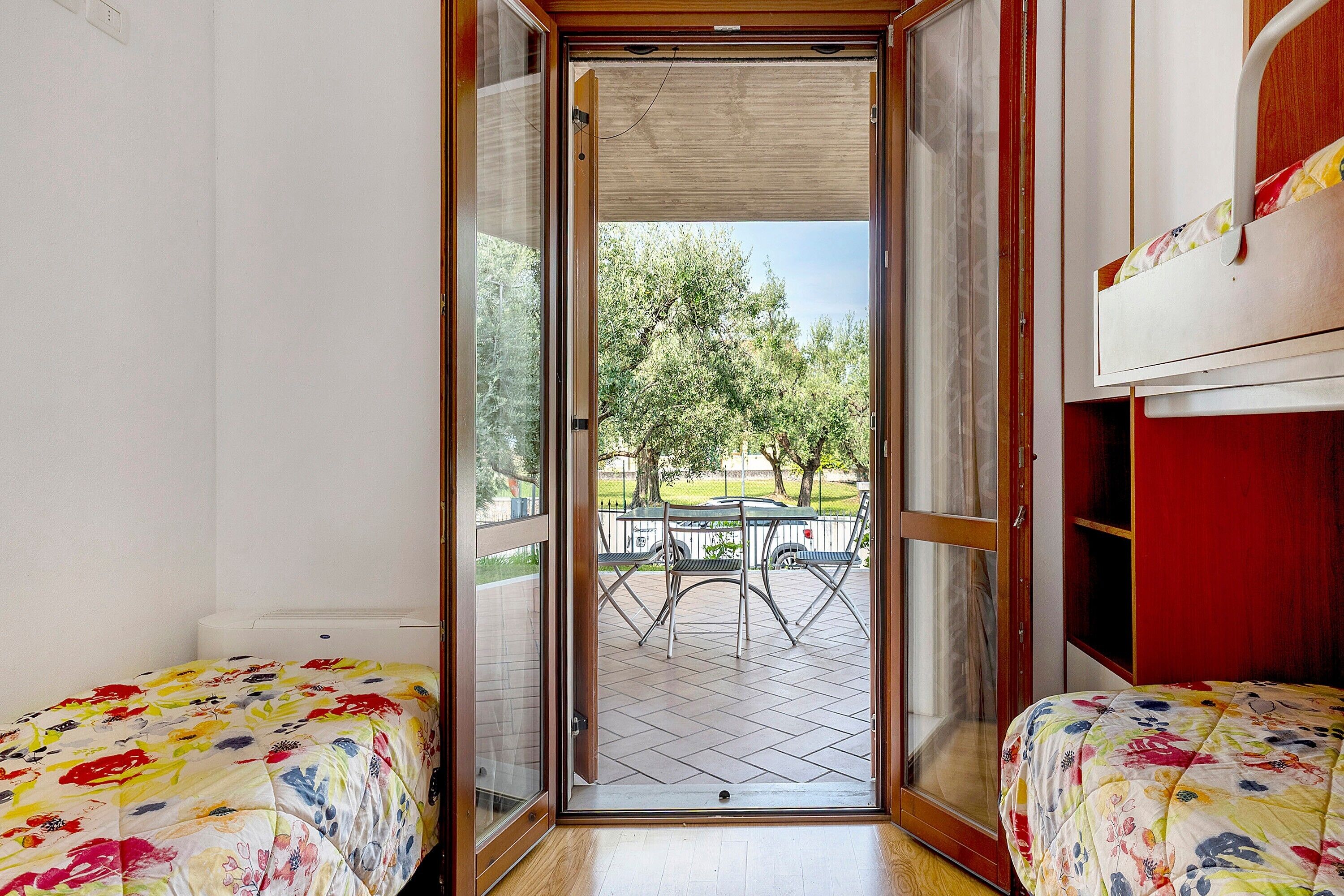 A room with a bed, a small table, and a view of an outdoor patio with a table and chairs.