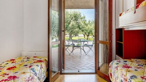 Una habitació amb un llit, una taula petita i vista a un pati exterior amb taula i cadires.