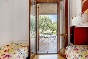 A room with a bed, a small table, and a view of an outdoor patio with a table and chairs. - Gigli Apartment with Garden, Shared Pool, Wi-Fi and Air Conditioning (Lazise)
