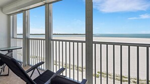 Een balkon met uitzicht op het strand en de oceaan, een tafel en twee stoelen.