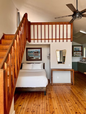 Ein Schlafzimmer mit einer Holztreppe, einem Bett, einem Deckenventilator, einem Gemälde und einer Küchenzeile.