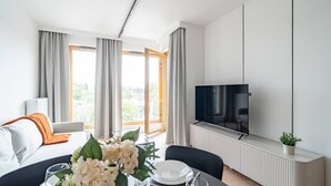 Een moderne hotelkamer met een zithoek, een flatscreen televisie aan de muur en grote ramen met gordijnen.