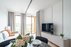 A modern hotel room with a dining area, a flat-screen TV mounted on the wall, and large windows with curtains. - Portowa M2 - Vistula River nearby, Parking, Balcony - by Rentujemy (Kraków)