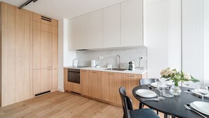 Een moderne keuken met houten kastjes, een inbouwvaatwasser en een eethoek met een tafel gedekt voor twee personen.