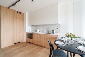 A modern kitchen with wooden cabinets, a built-in dishwasher, and a dining area with a table set for two. - Portowa M2 - Vistula River nearby, Parking, Balcony - by Rentujemy (Kraków)