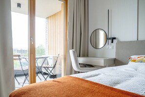 A hotel room with a bed, a desk, a chair, a mirror, and a view of the outdoors. - Portowa M2 - Vistula River nearby, Parking, Balcony - by Rentujemy (Kraków)