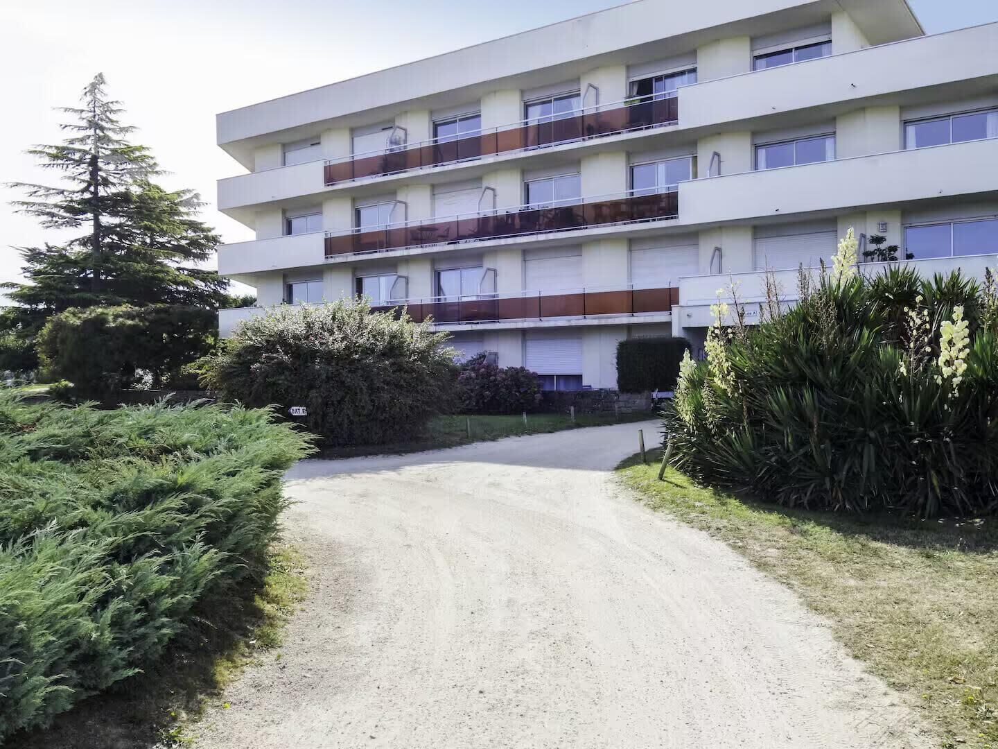 Un edificio a più piani con un ingresso centrale, circondato da vegetazione e un vialetto sterrato.