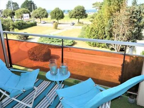Ein Balkon mit blauen Stühlen und einem Tisch, mit Blick auf eine Straße und Grünflächen.