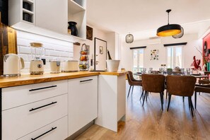 A modern kitchen with white cabinets, a wooden countertop, and a dining area with brown chairs. - Luxury Rooftop Duplex | Terrace, Views & Parking (Lisboa)