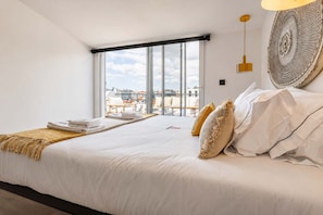 A hotel room with a large bed, a view of the city through a window, and a decorative wall piece. - Luxury Rooftop Duplex | Terrace, Views & Parking (Lisboa)