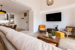 A modern living room with a sofa, chairs, a coffee table, and a flat-screen TV mounted on the wall. - Luxury Rooftop Duplex | Terrace, Views & Parking (Lisboa)