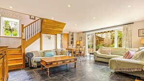 A spacious living area with a wooden staircase, a sofa set, a dining table, and a large window with curtains. - The Stag in the Chiltern Hills (Fawley)