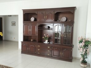Um armário de madeira escura com vários compartimentos e gavetas, um vaso com flores e uma planta em vaso.