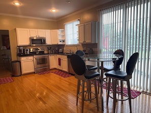 A modern kitchen with white cabinets, stainless steel appliances, and a glass dining table with four chairs. - Spacious 3-Bedroom House in Pittsfield Township – Close to U of M & EMU (Ypsilanti)