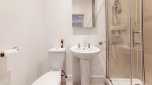 Une salle de bain équipée de toilettes, d’un lavabo, d’un miroir et d’une douche à parois en verre.