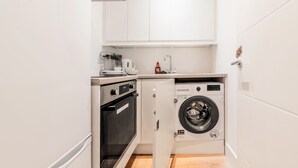 Une cuisine compacte équipée d’un four encastré, d’un lave-linge et d’une machine à café.
