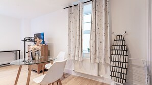Une pièce moderne avec une table en verre, des chaises blanches, un radiateur et un étendoir.