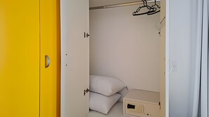 An open wardrobe with a hanging rod, a shelf with pillows, and a small cabinet. - SHB - Entre a Praia e o Mundo Disney (Santos)