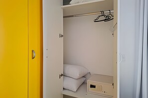 An open wardrobe with a hanging rod, a shelf with pillows, and a small cabinet. - SHB - Entre a Praia e o Mundo Disney (Santos)