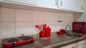A kitchen with white cabinets, a granite countertop, a red induction cooktop, and a red laundry basket. - SHB - Entre a Praia e o Mundo Disney (Santos)