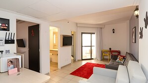 A modern living room with a white sofa, a red rug, and a dining area with a table and chairs. - SHB - Entre a Praia e o Mundo Disney (Santos)