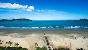 A beach with a long pier extending into the ocean, surrounded by sandy areas and palm trees. - SHB - Entre a Praia e o Mundo Disney (Santos)
