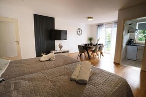 Una habitación de hotel con una cama grande, un televisor montado en la pared, una zona de comedor con sillas y una cocina.