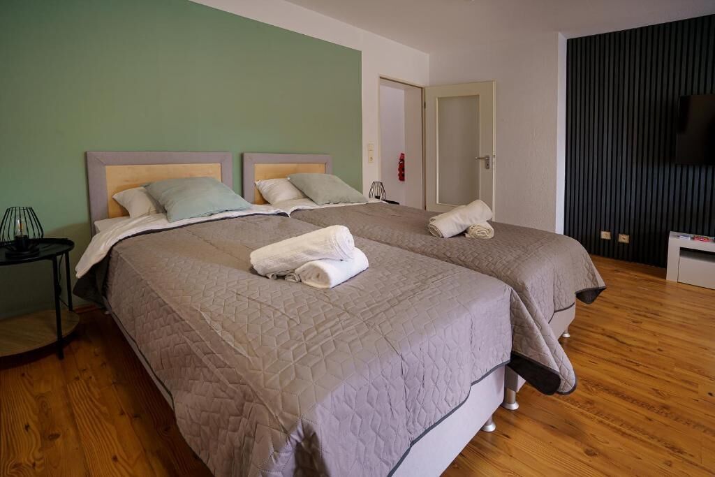 A hotel room with two beds, a bedside table, a lamp, and a TV.