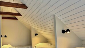 Une petite chambre mansardée avec deux lits superposés, des poutres en bois et des luminaires fixés au mur.