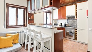 A compact kitchen with a central island, wooden cabinets, a built-in microwave, and a gas stove. - GuestReady - Casa Âncora (Aveiro)