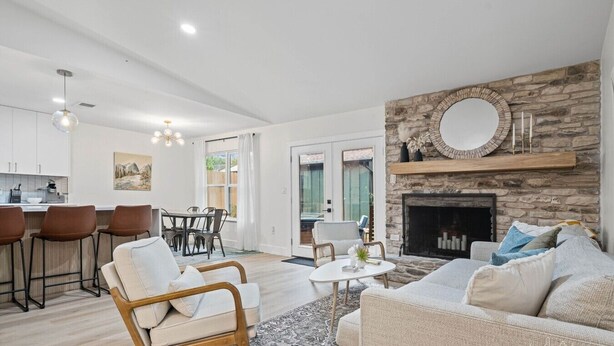 A modern living room with a stone fireplace, a dining area with bar stools, and a kitchen visible through an open door. - Game, Grill & Lounge Modern S Austin Hangout House Sleeps 10 - Mins to SoCo (Austin)