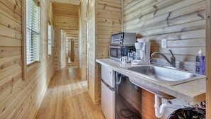 A wooden interior with a kitchen area featuring a sink, a coffee maker, and a microwave.