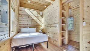A wooden cabin bedroom with a bed, a nightstand, a lamp, and a window.